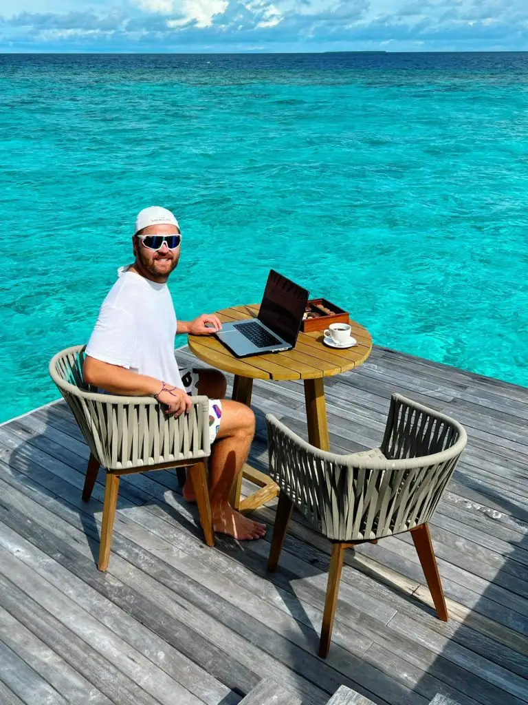 Man working on a laptop by the ocean, embodying remote work lifestyle.